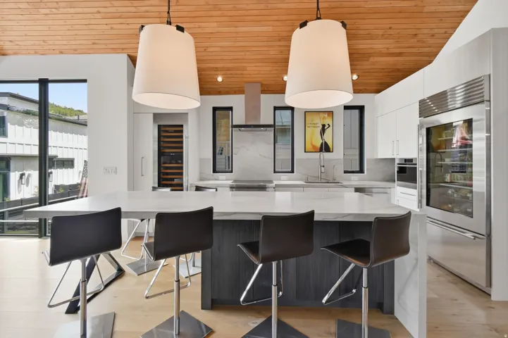 Contemporary kitchen featuring a large central island with seating, a visible wine refrigerator, and stainless steel built-in appliances