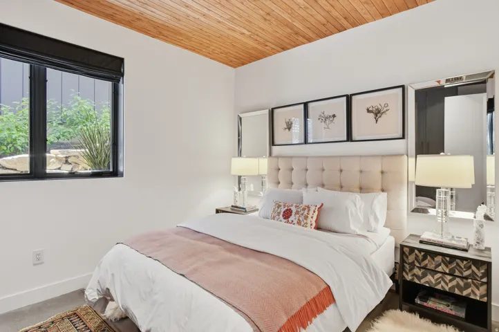 Bedroom featuring a wood-panel ceiling, dark-framed window, and light-toned wall