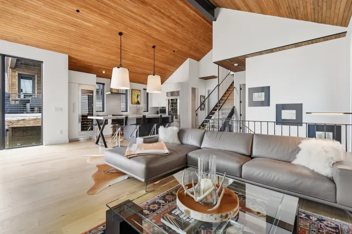 Open-concept living area featuring a vaulted wood-paneled ceiling, light wood-finish flooring, and a modern kitchen with a large island