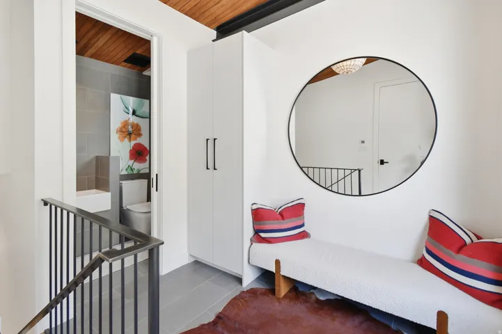Modern hallway featuring a circular black-framed mirror, built-in white cabinetry, and a wood-paneled ceiling