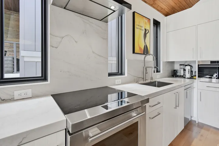 Modern kitchen featuring white cabinetry, stone-finish countertops, and a stainless steel cooktop with a built-in oven