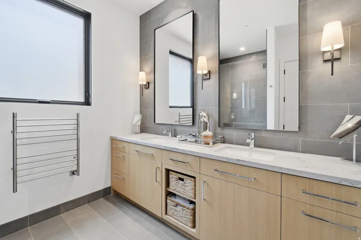 Modern bathroom featuring a dual vanity with light wood-finish cabinetry, white countertops, and undermount sinks