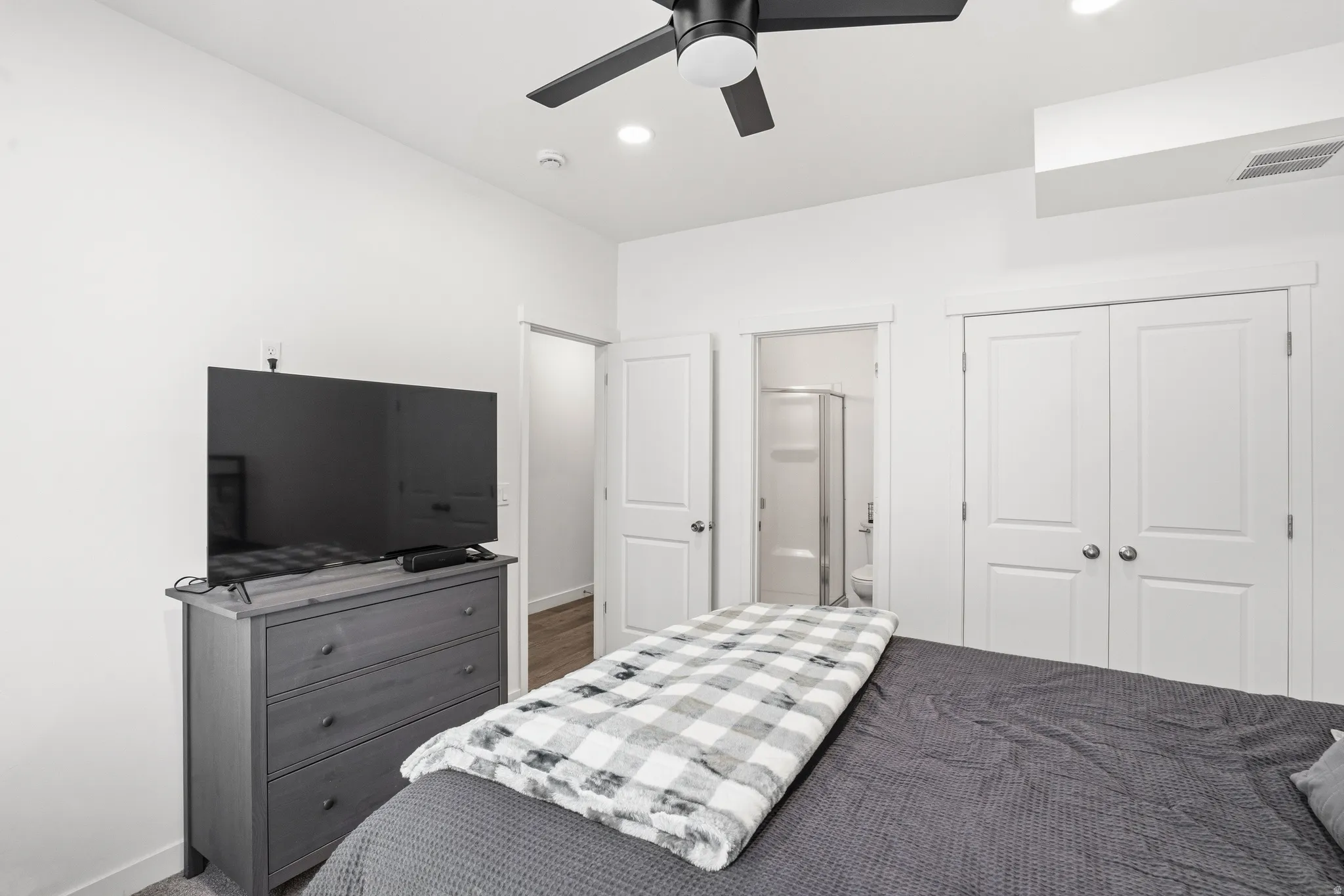 White painted walls and trim throughout, featuring a black ceiling fan with integrated lighting, recessed ceiling lighting, and a double-door closet with chrome hardware