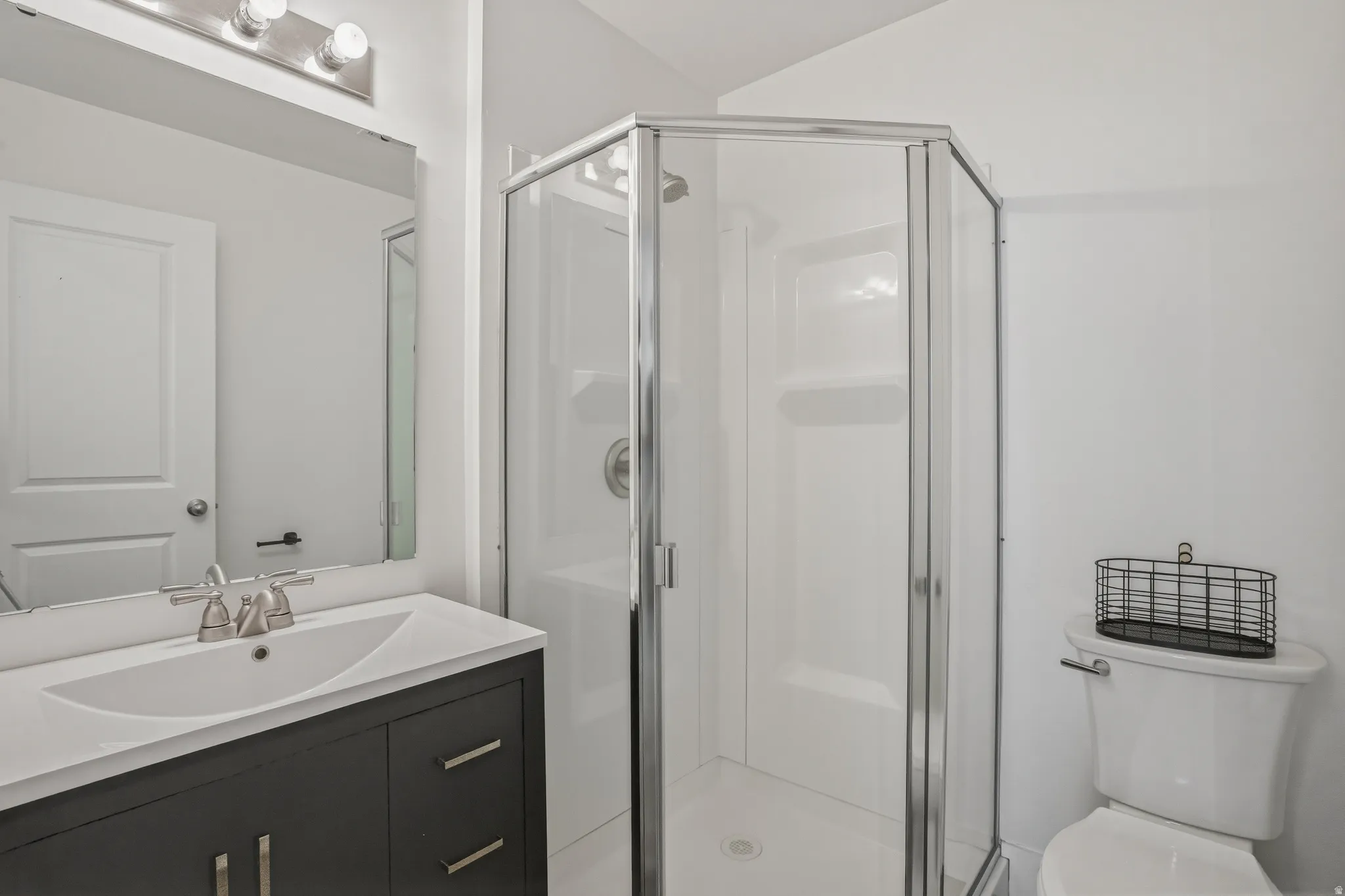 Bathroom featuring a glass-enclosed shower, dark wood-finish vanity with a white countertop, undermount sink, and brushed nickel fixtures