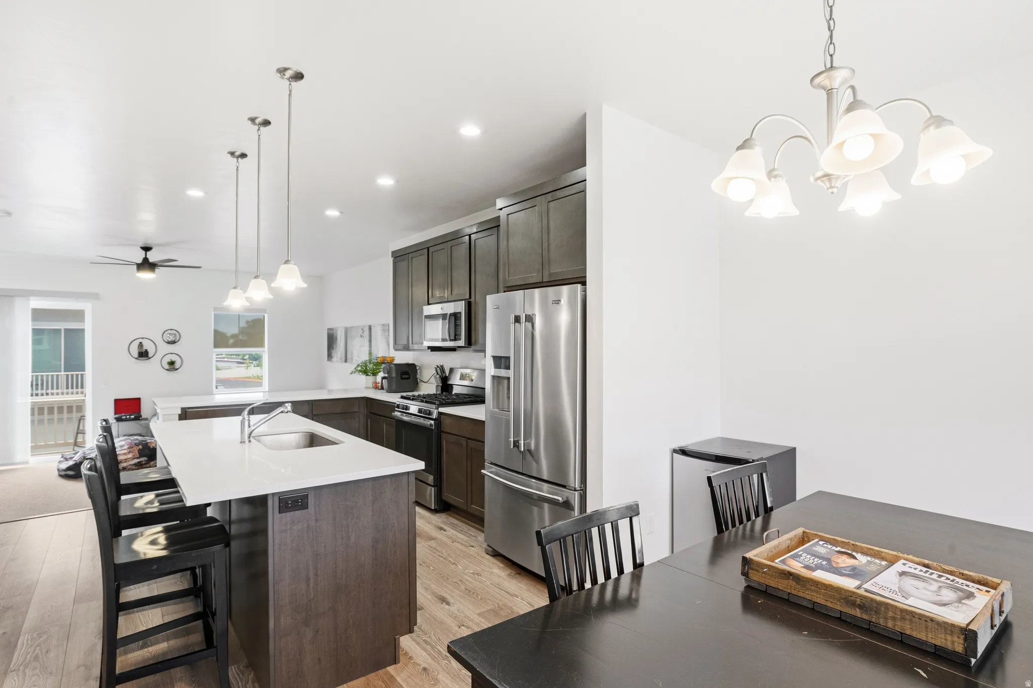 Modern kitchen featuring stainless steel appliances, dark wood-finish cabinetry, a large center island with a sink, pendant lighting, and wood-finish flooring