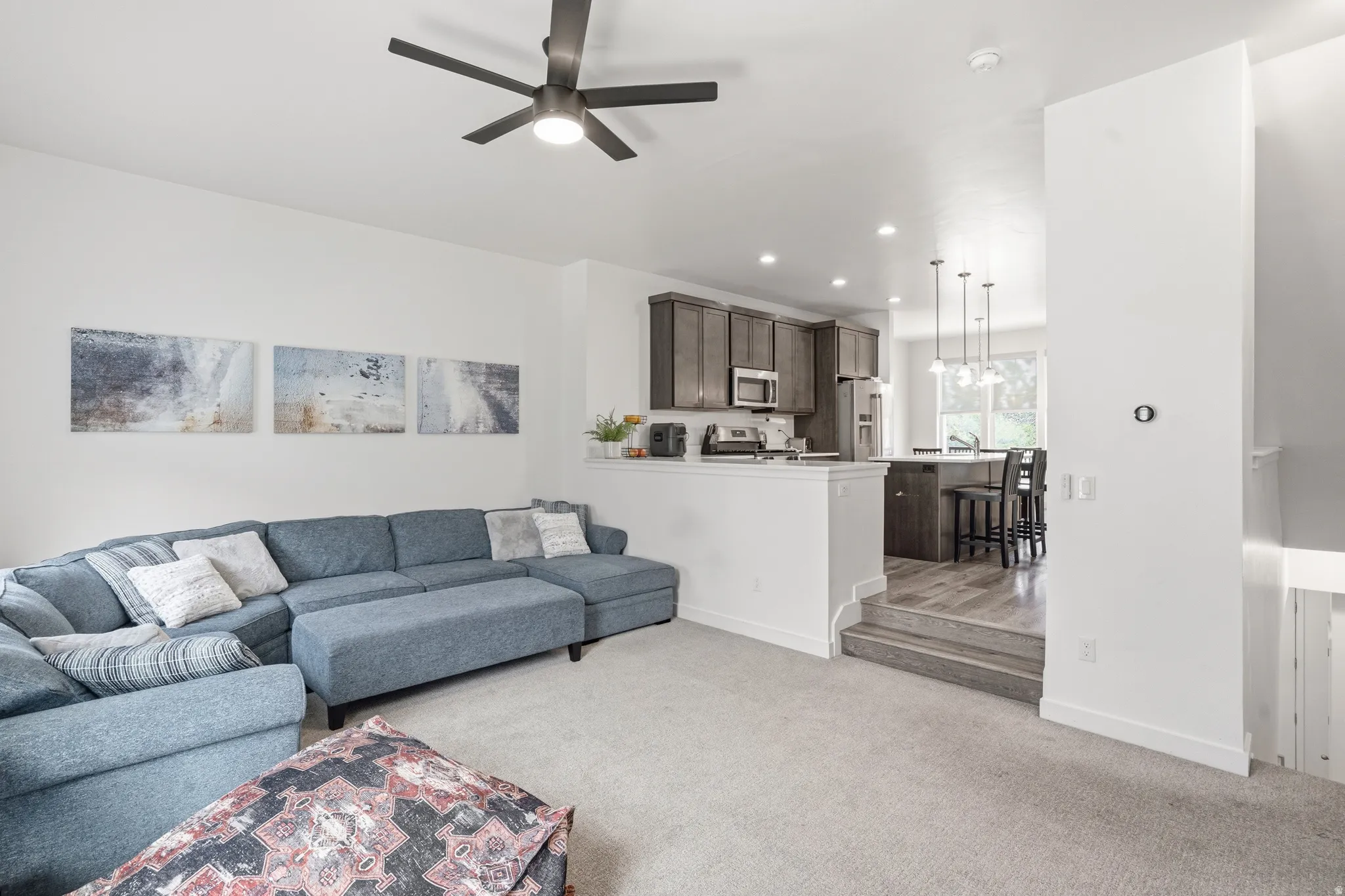 Open-concept living area with light-colored carpeting, a dark-toned ceiling fan, and recessed lighting
