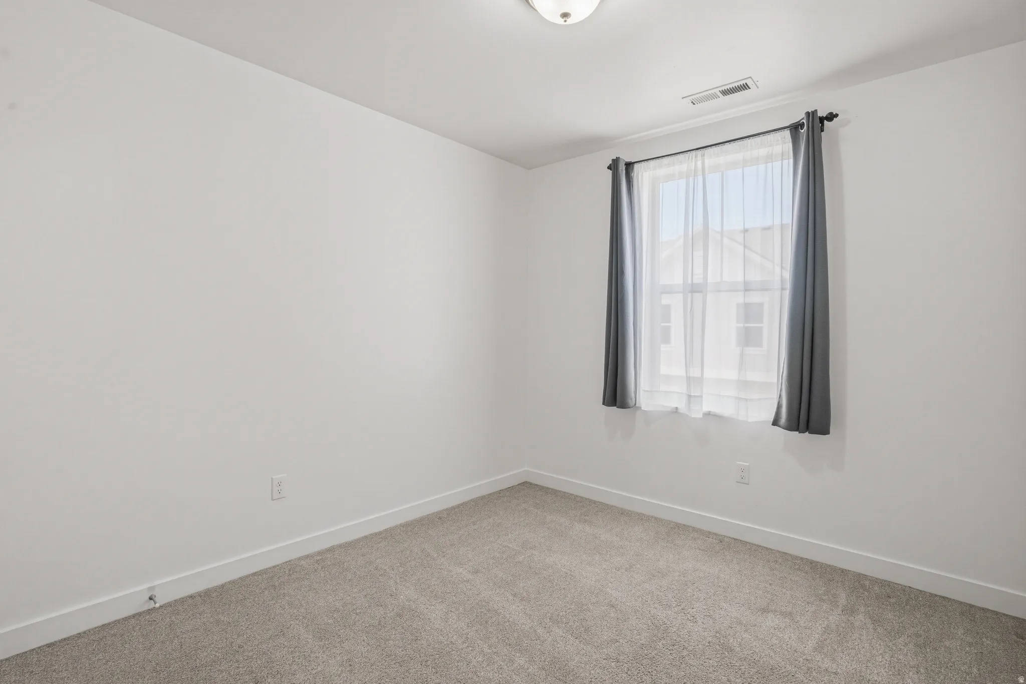 Carpeted room featuring a single window with curtain rod and drapes, white walls, and a ceiling-mounted light fixture