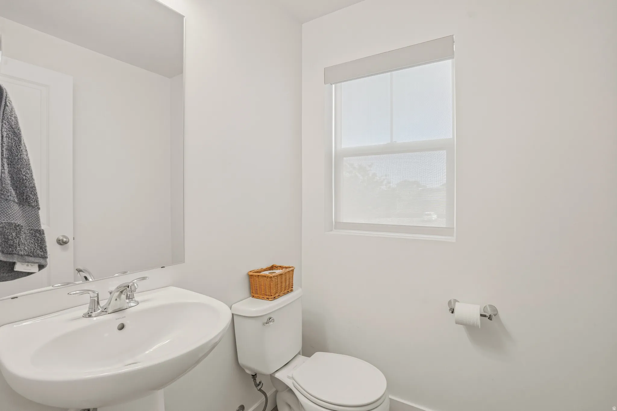 Pedestal sink with chrome faucet, large frameless mirror, and neutral wall paint