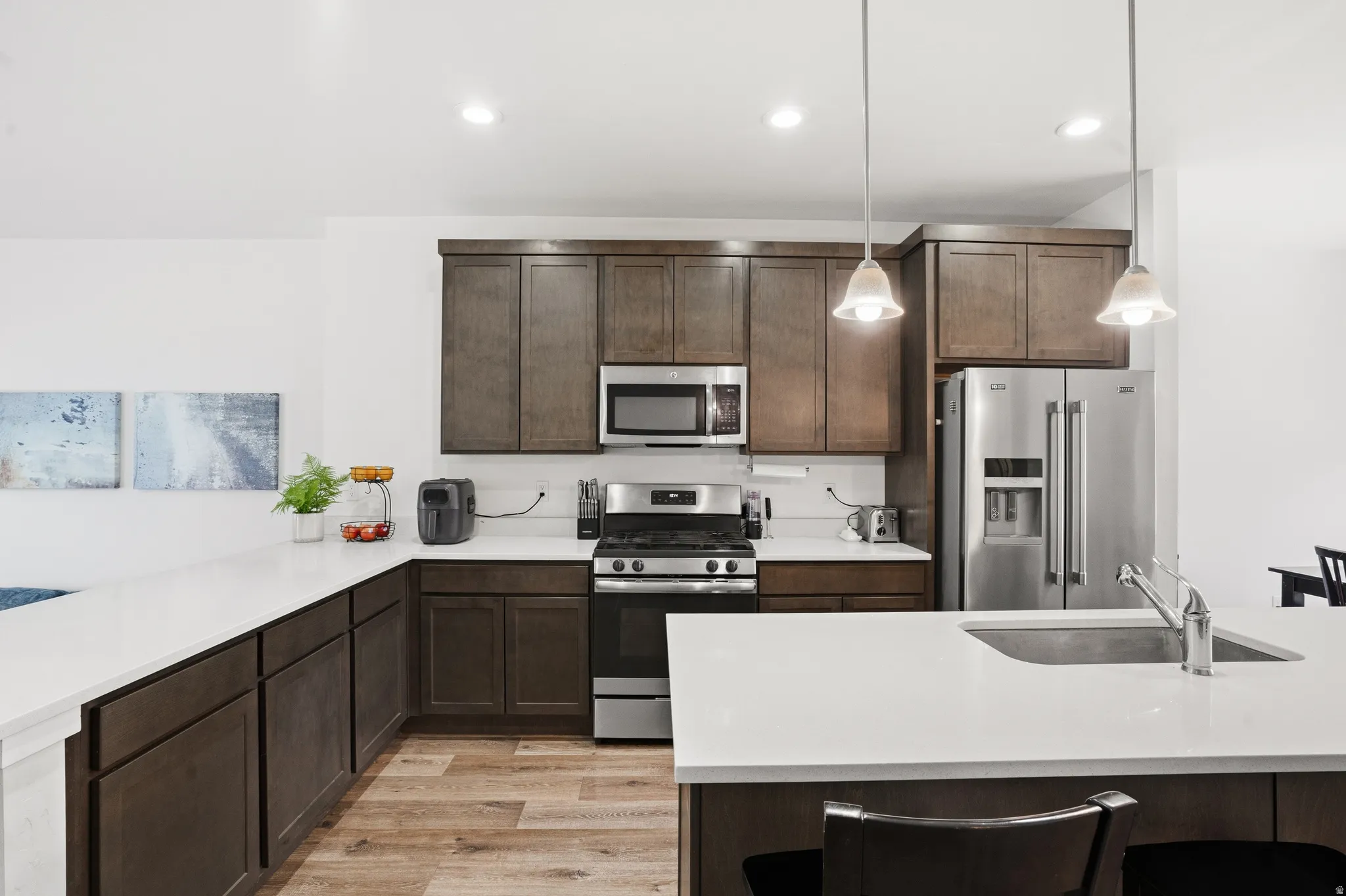 Kitchen featuring dark wood-finish cabinetry, stainless steel appliances, white countertops, and wood-finish flooring