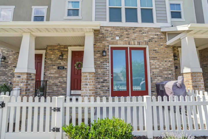 Brick facade townhome with a white picket fence, covered front porch, red entry door, and red-framed glass patio doors