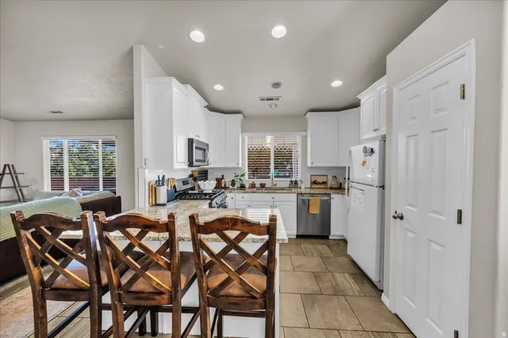 Kitchen featuring white cabinetry, a large kitchen island with a stone countertop, stainless steel dishwasher, a built-in microwave, and tile flooring