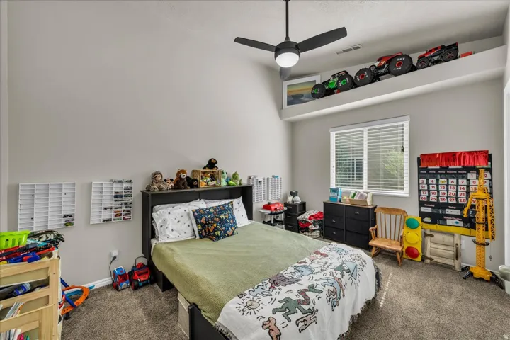 Room featuring a vaulted ceiling with a built-in display shelf, a ceiling fan, window with blinds, and carpet flooring