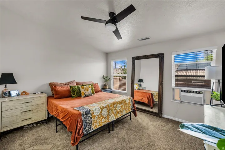 Carpeted bedroom featuring a ceiling fan with integrated lighting, multiple windows with blinds, and white walls