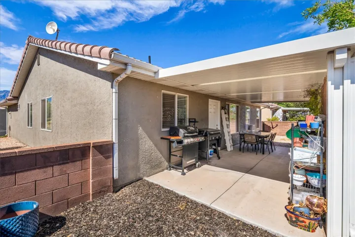 Expansive concrete patio area with a white aluminum patio cover, featuring stucco exterior siding and a red tile roofline