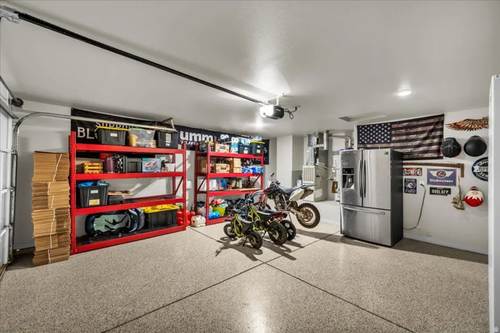 Spacious garage featuring a durable epoxy floor coating, extensive red metal shelving, overhead lighting, an exposed garage door track, and a ceiling-mounted garage door opener
