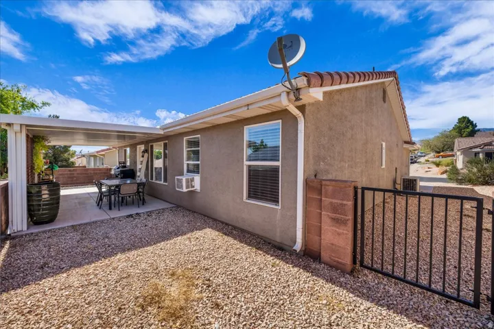 Rear exterior featuring a covered patio with a concrete slab, stucco siding, and a gravel yard