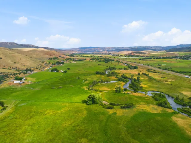 Expansive green landscape featuring a winding river, distant hills, and a prominent highway