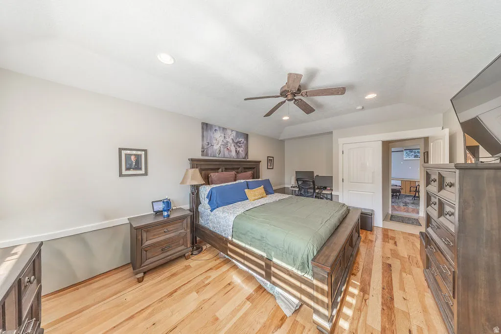 Spacious bedroom featuring wood-finish flooring, a tray ceiling with recessed lighting, and a ceiling fan
