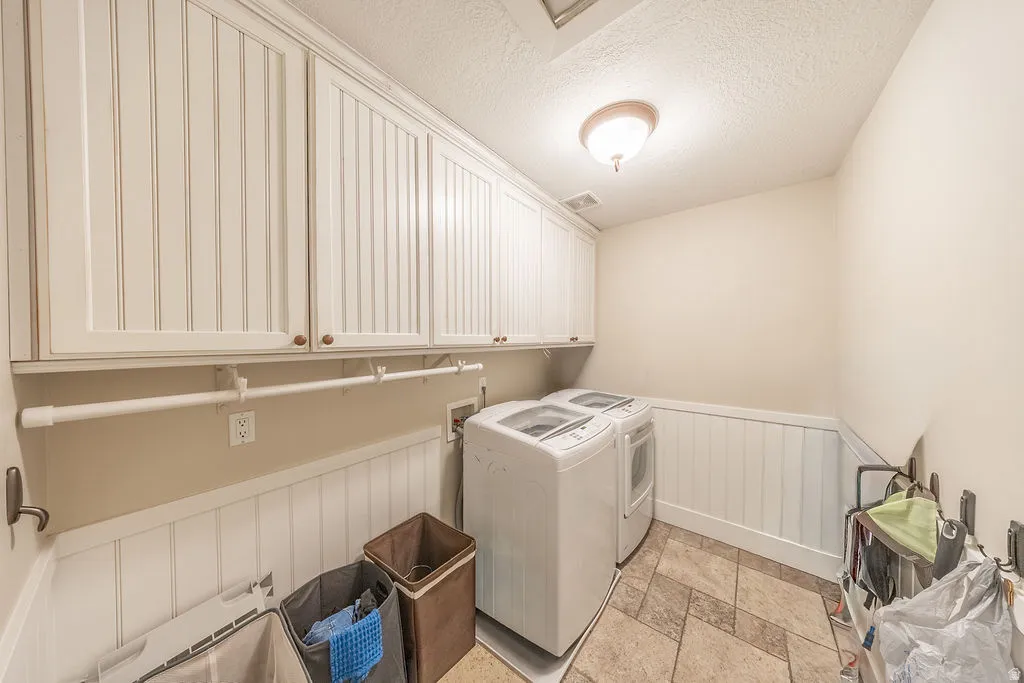 Laundry area featuring beadboard wainscoting, upper cabinetry with wood-finish knobs, and neutral-toned tile flooring