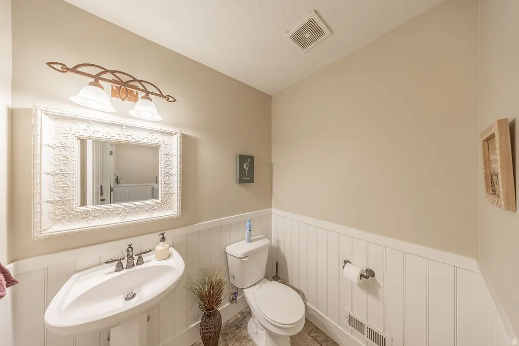 Pedestal sink with polished chrome fixtures, framed mirror with ornate detailing, and a two-light vanity fixture