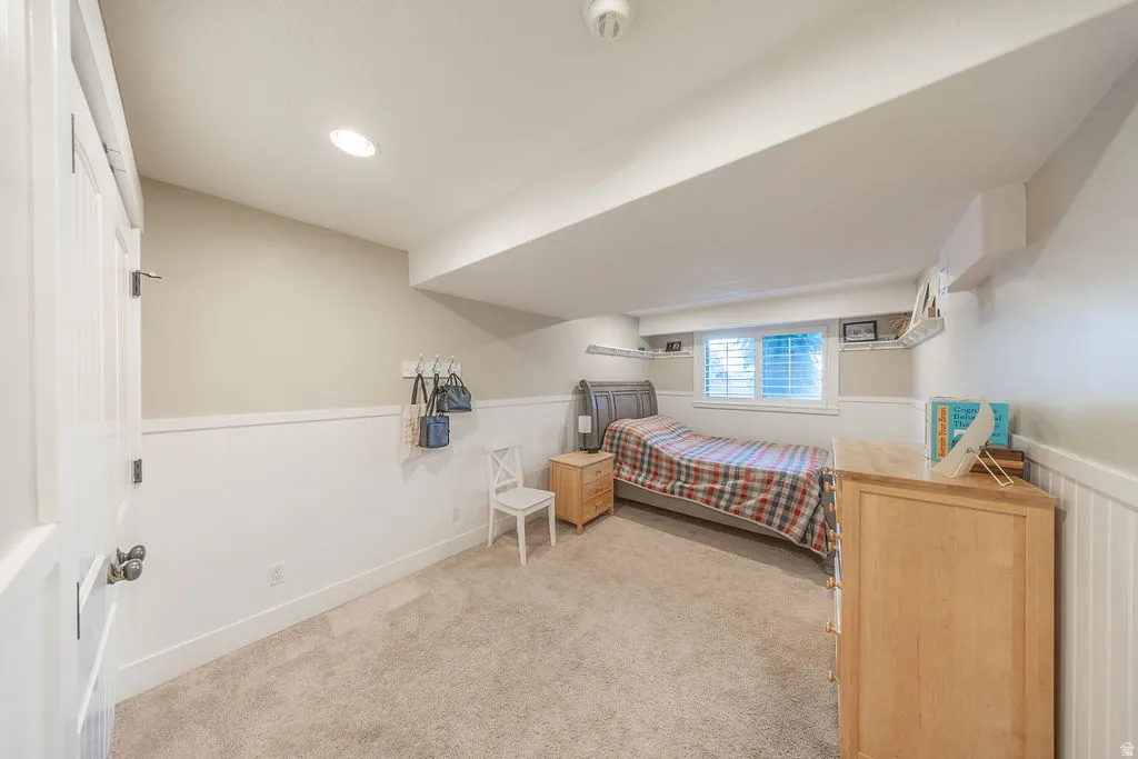 Carpeted room featuring a white paneled door with dark hardware, recessed lighting, a window with horizontal blinds, and wainscoting