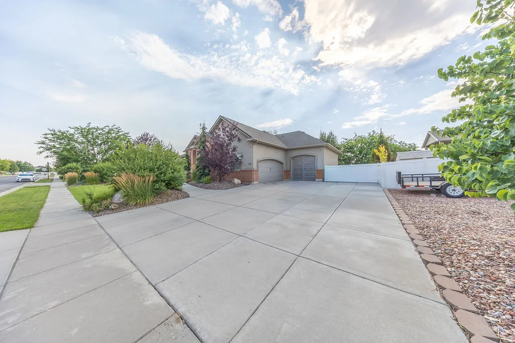 Concrete driveway with a two-car garage, manicured shrubbery, established trees, and a white privacy fence