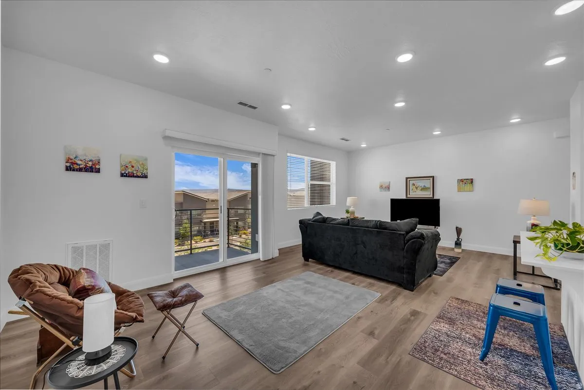 Open-concept living space with wood-finish flooring, recessed lighting, and a sliding glass door to a private balcony