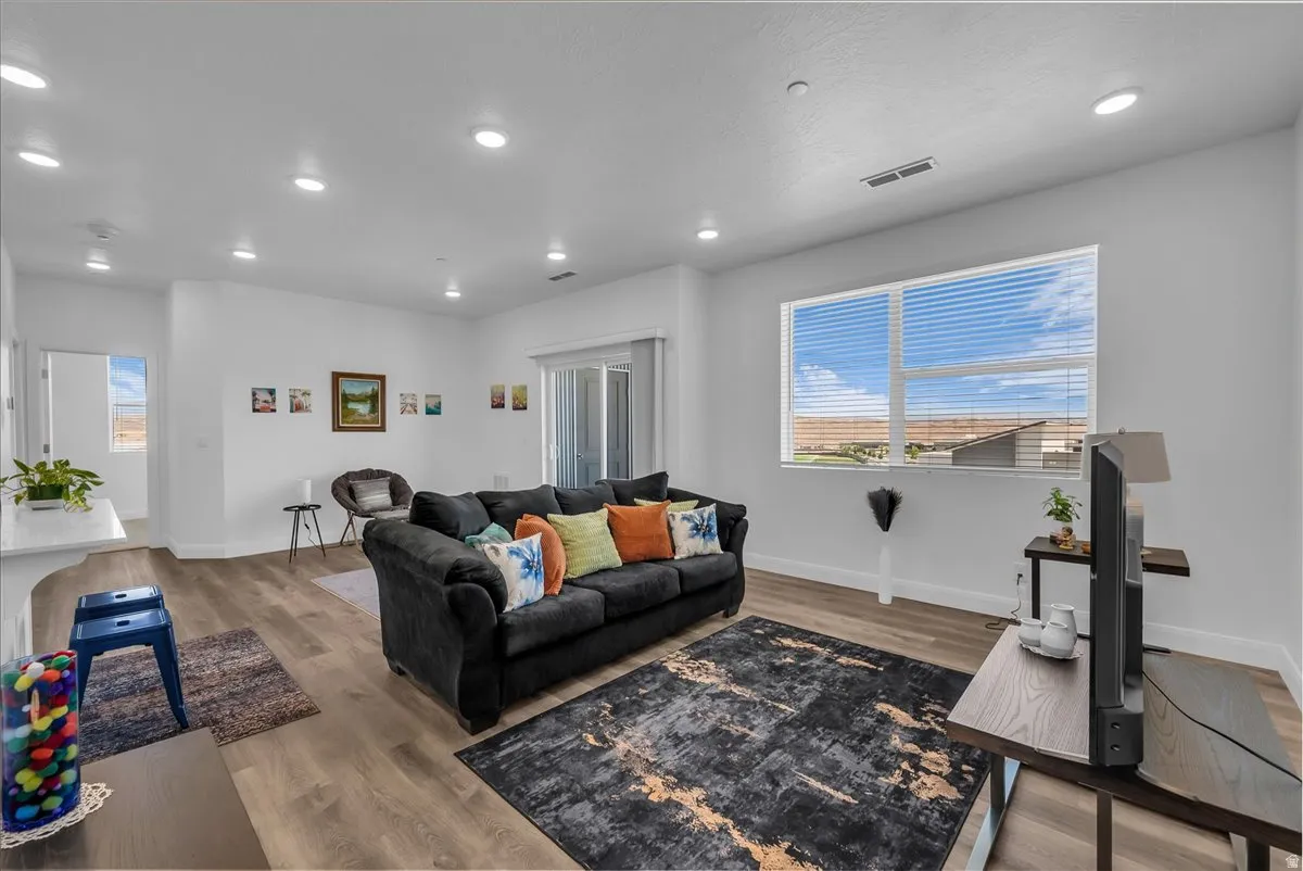 Spacious living area featuring large windows with blinds, wood-finish flooring, recessed lighting, and a sliding glass door