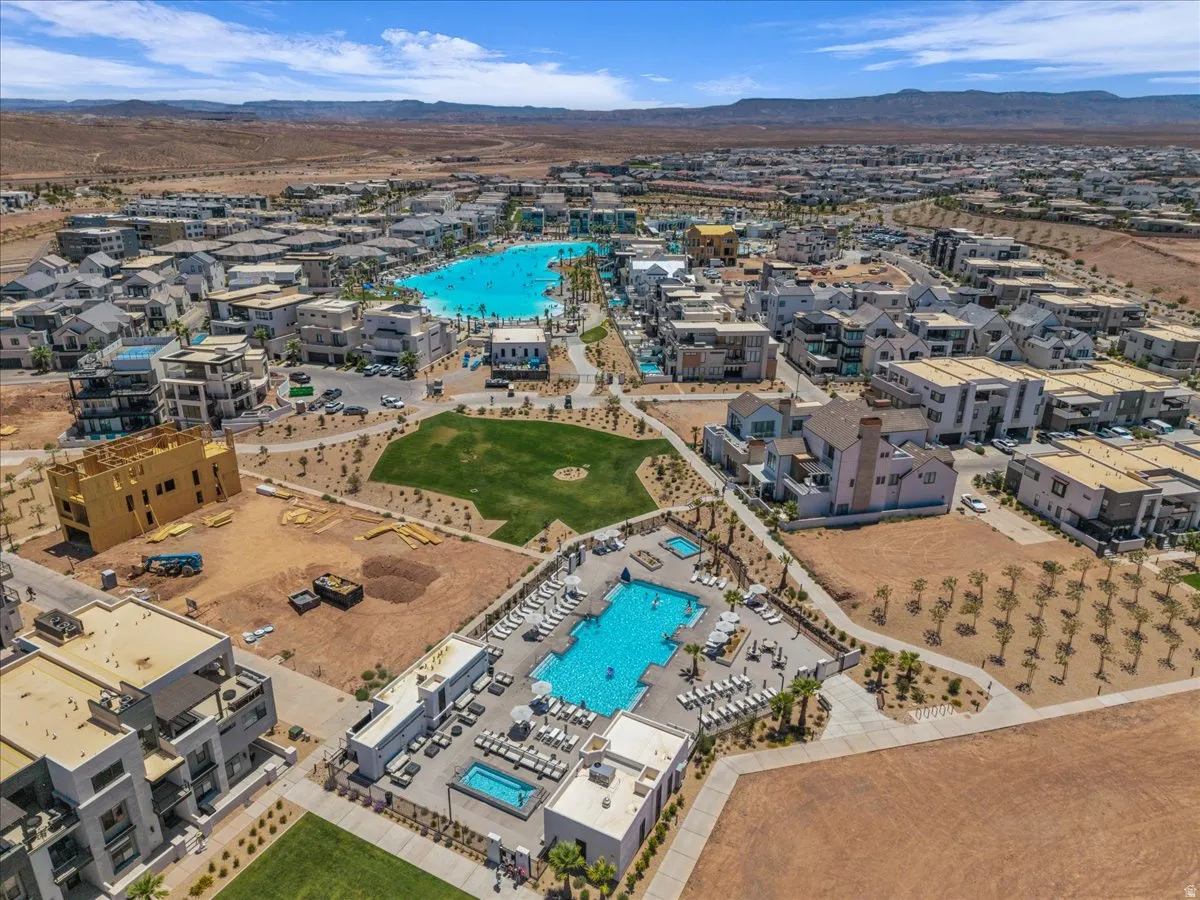 Expansive aerial view of a community featuring a large turquoise lagoon, a separate resort-style swimming pool area with numerous lounge chairs, and a central green space