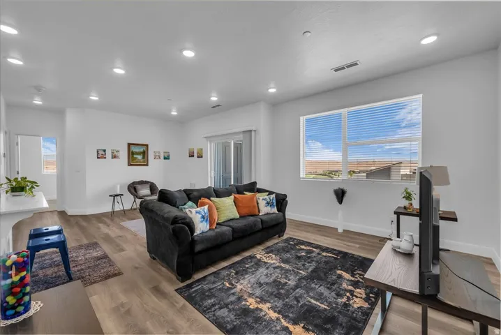 Spacious living area featuring large windows with blinds, wood-finish flooring, recessed lighting, and a sliding glass door