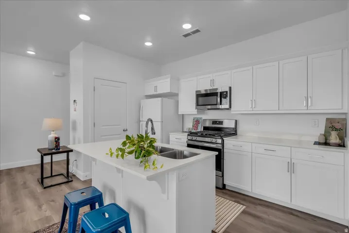 Modern kitchen featuring white shaker cabinetry, stainless steel appliances, a center island with an undermount double sink, white countertops, and wood-finish flooring
