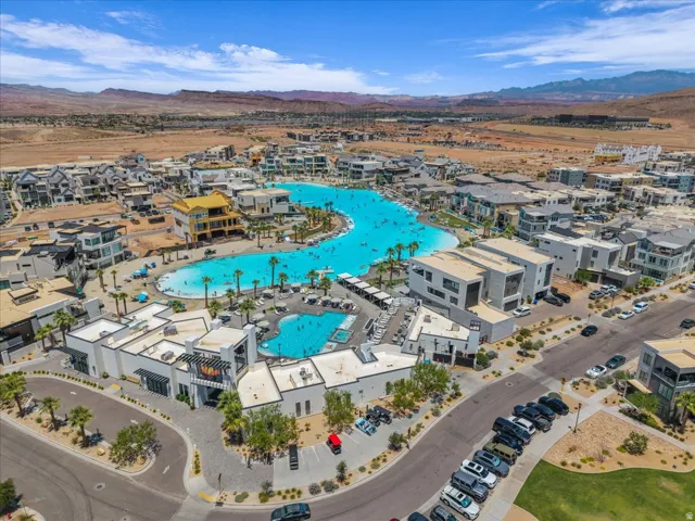 Expansive community featuring a large, blue artificial lagoon with multiple swimming areas, a surrounding sand-toned beach, and various structures including multi-story buildings with balconies