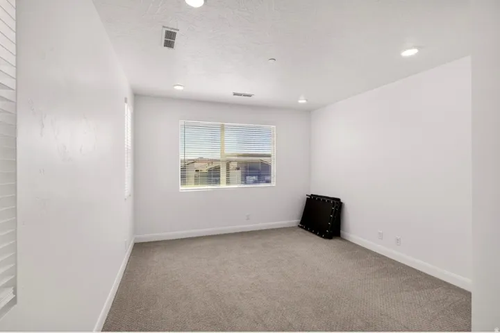 Carpeted room featuring a large window with horizontal blinds, recessed lighting, and white baseboards