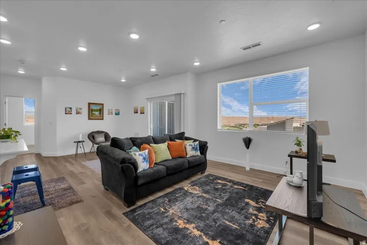 Spacious living area featuring neutral white walls, wood-finish flooring, recessed lighting, and a large window with horizontal blinds