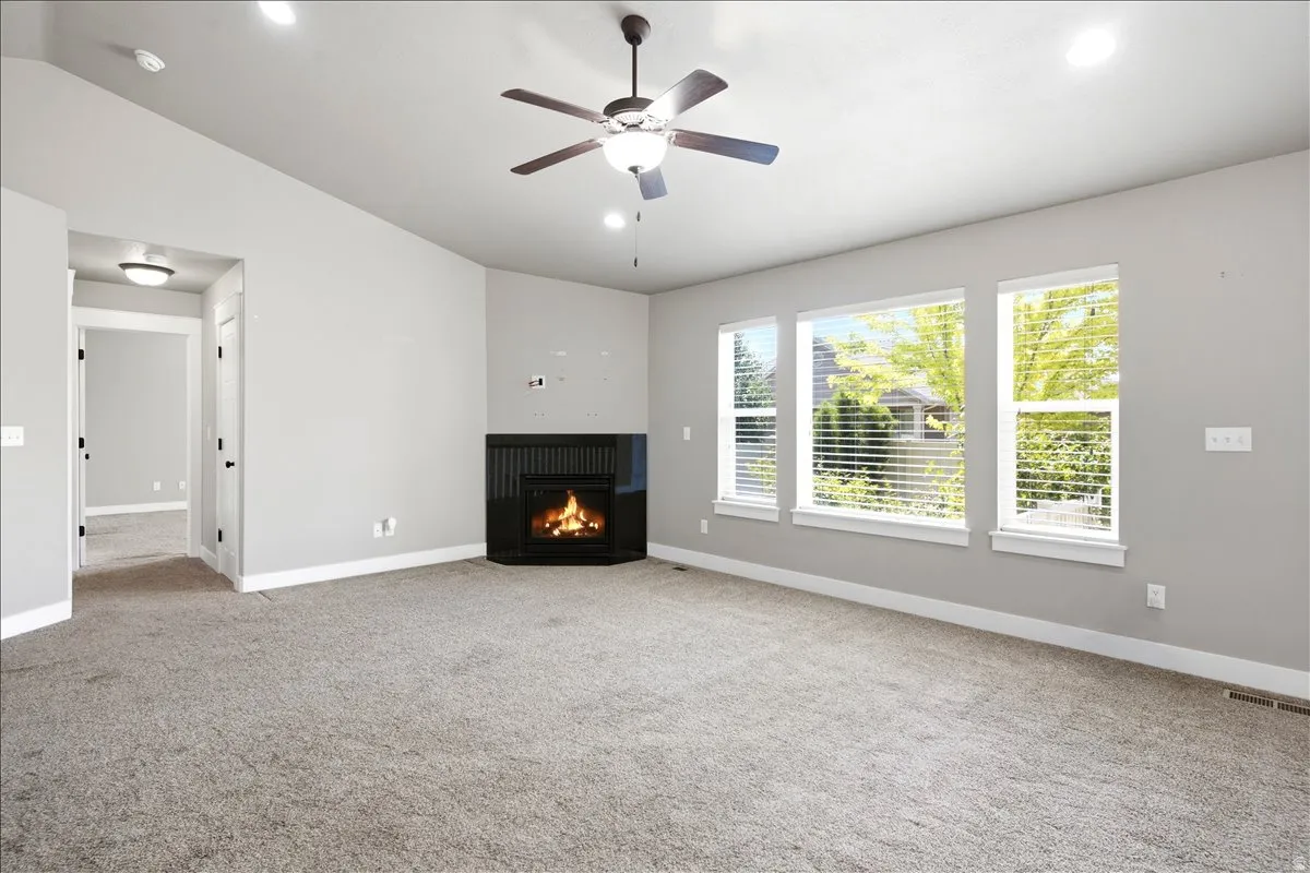 Spacious room featuring a corner fireplace with a dark mantel, multiple windows with blinds, recessed lighting, and a ceiling fan