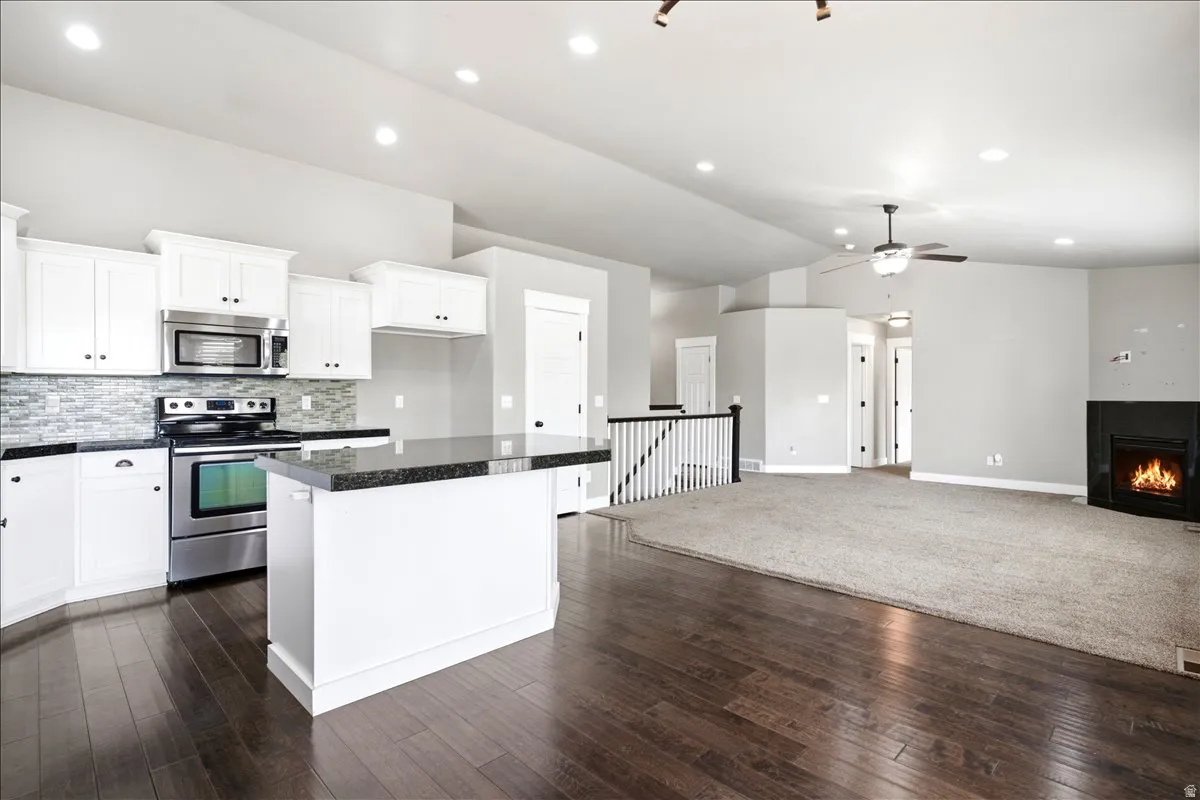 Open-concept living space featuring a kitchen with white cabinetry and dark countertops, stainless steel appliances, a tile backsplash, and a central island
