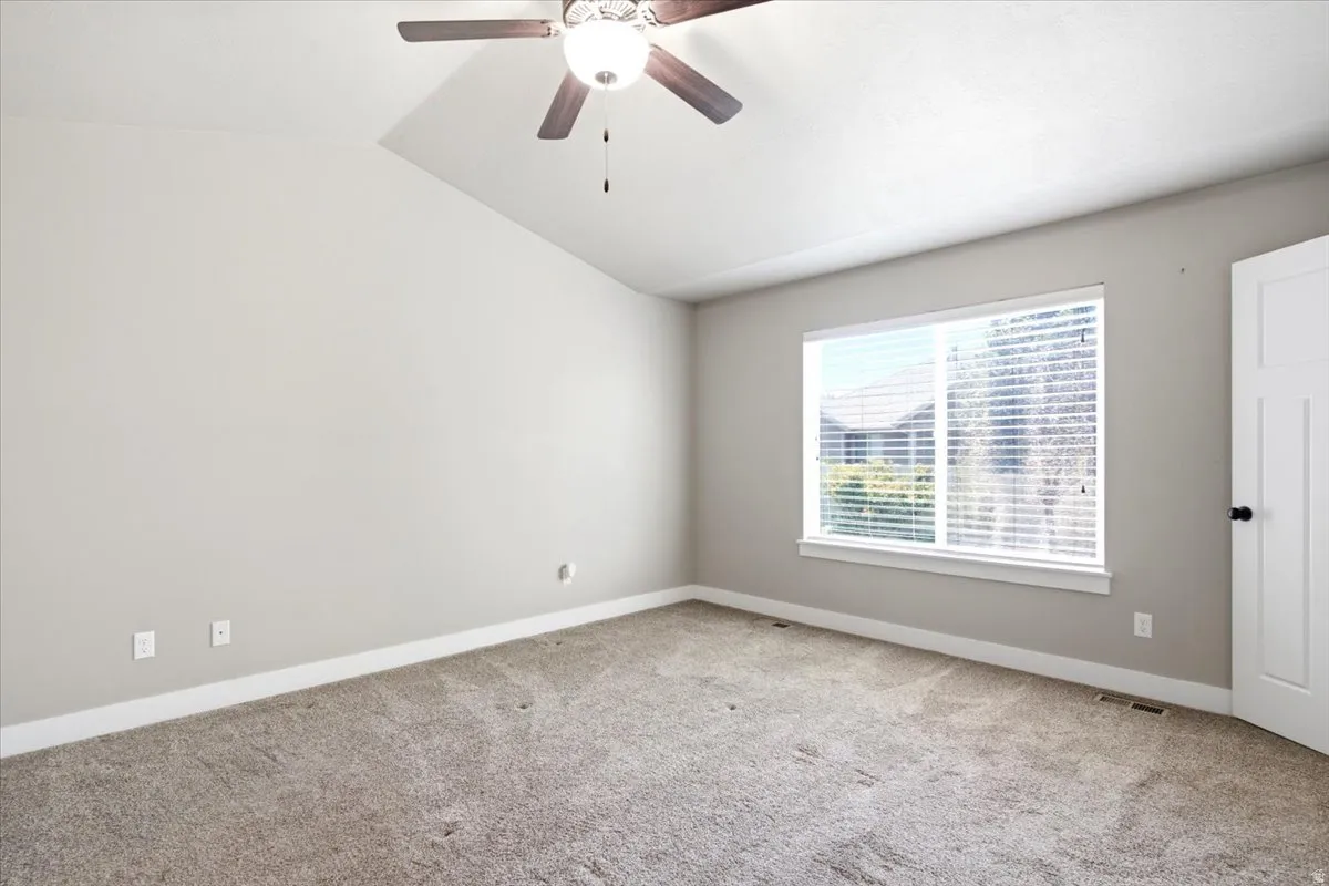Interior room featuring a vaulted ceiling with a ceiling fan, a large window with horizontal blinds, neutral wall paint, and carpet flooring