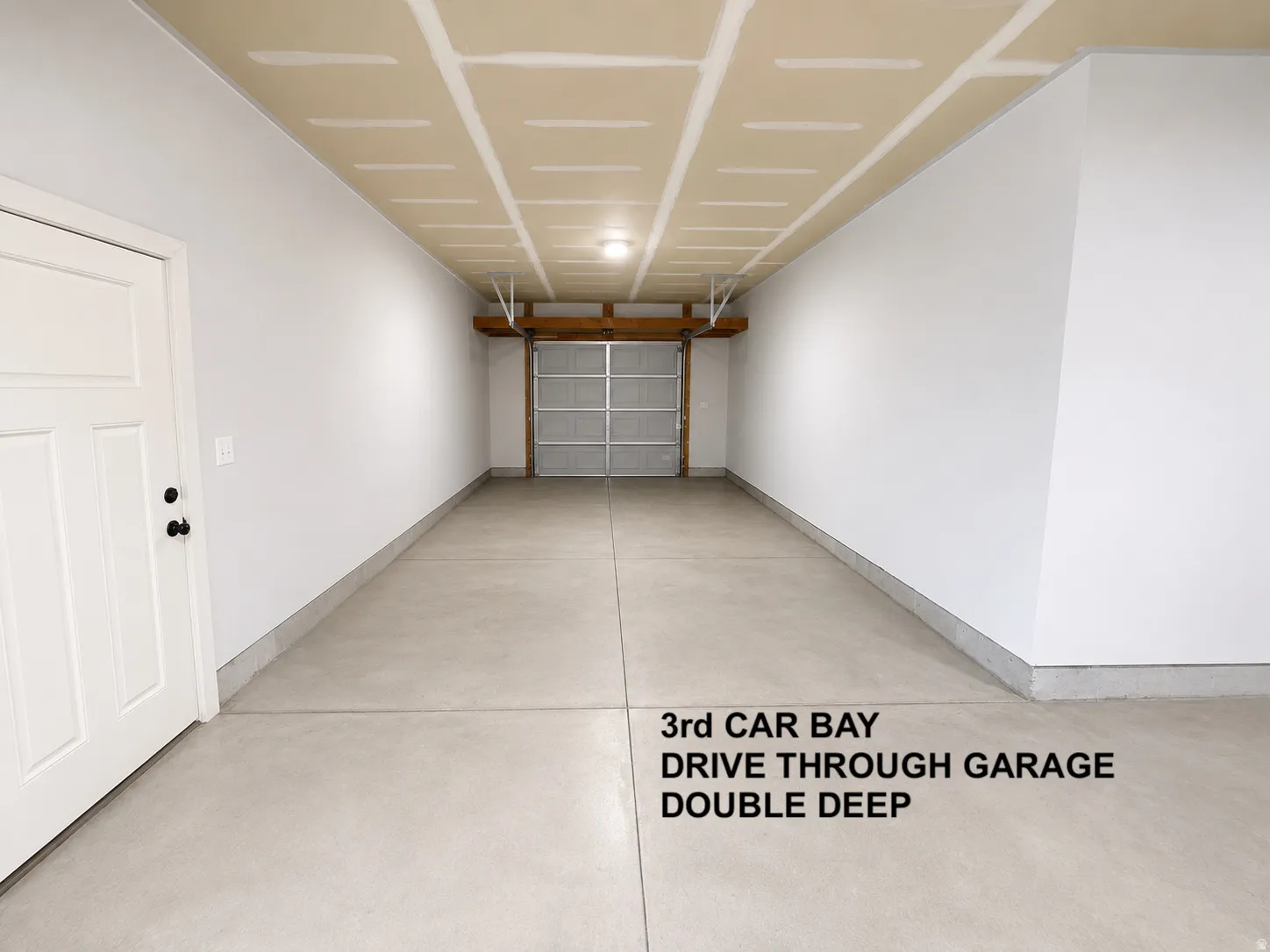 Spacious garage featuring a concrete floor, white painted walls, exposed ceiling joists, and a sectional garage door