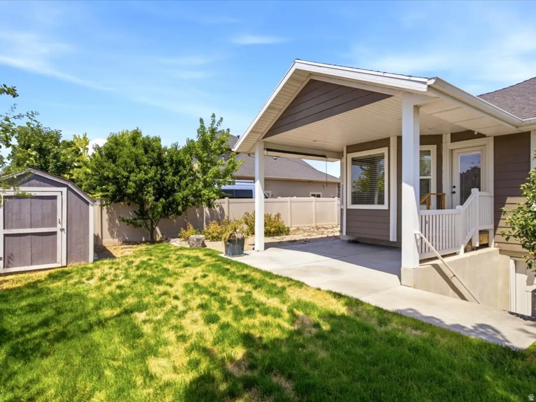 Expansive backyard featuring a covered patio, concrete walkway, and a detached storage shed