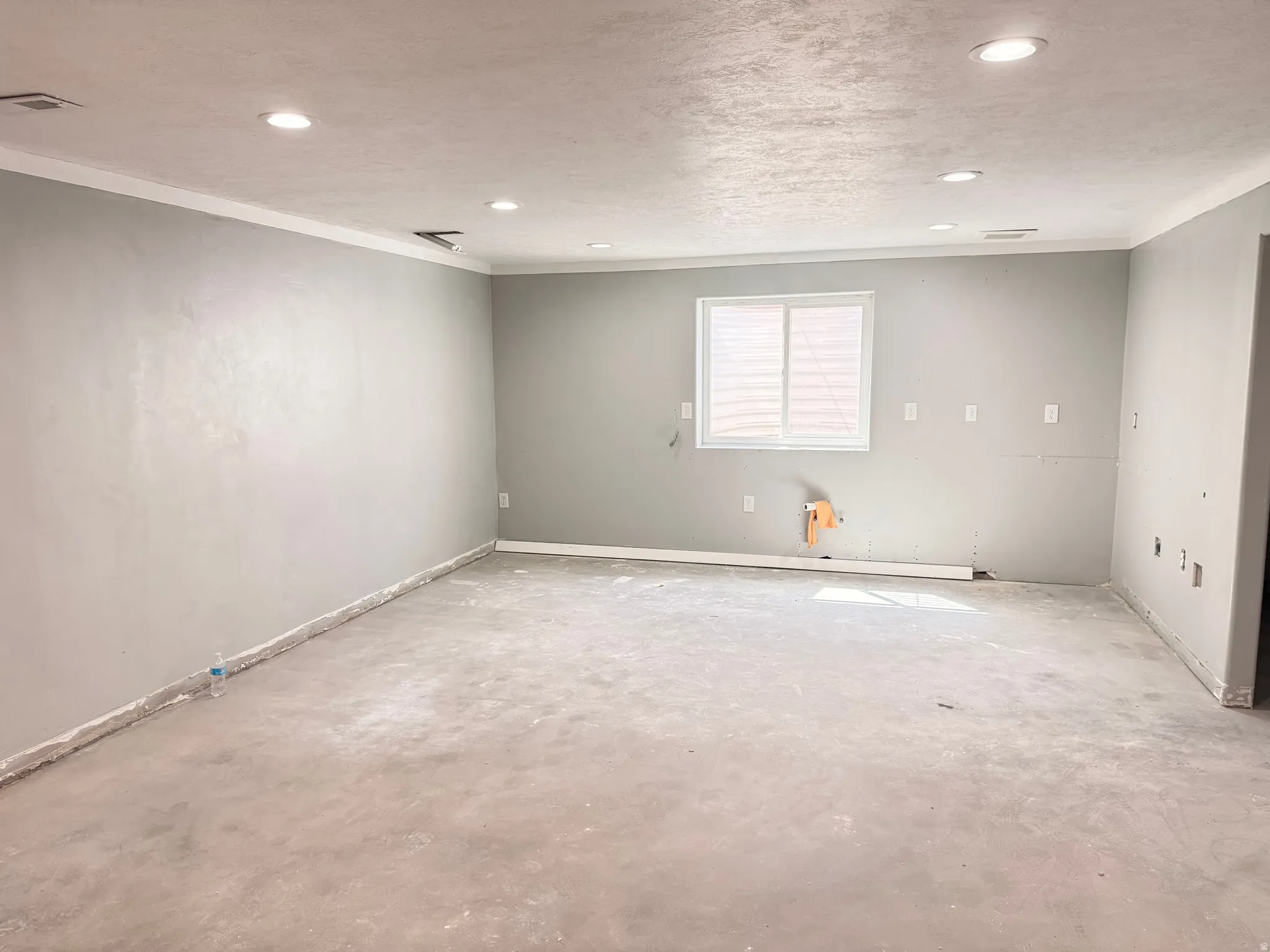 Recessed ceiling lighting, window with blinds, light gray wall finish, and raw concrete flooring