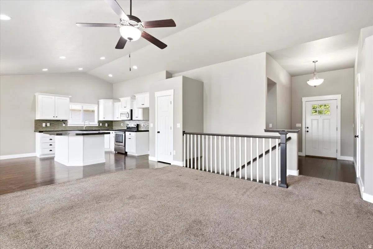 Open-concept living space featuring a kitchen with white cabinetry, dark countertops, and stainless steel appliances