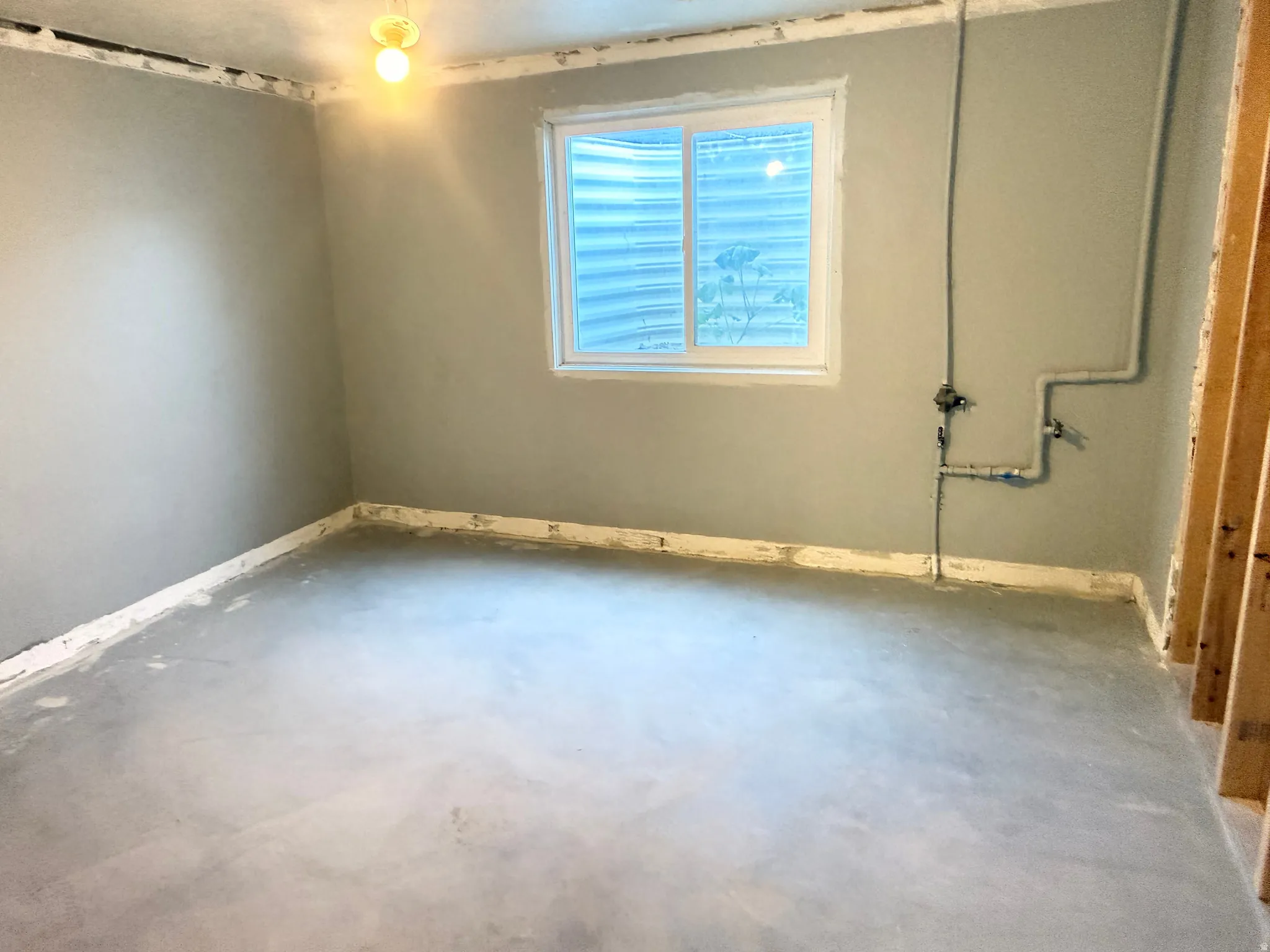 Concrete floor, single-pane window, exposed wall studs, and overhead light fixture