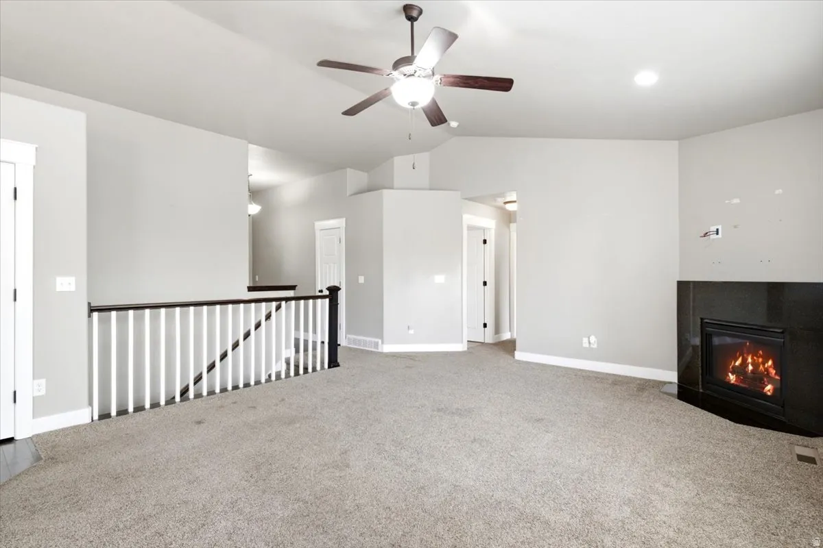 Spacious interior room featuring a corner fireplace with a dark surround, vaulted ceiling, and a ceiling fan with integrated lighting