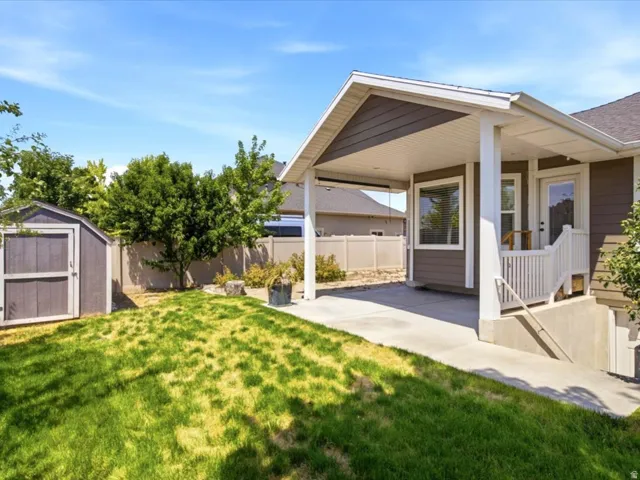 Expansive backyard featuring a covered patio, concrete walkway, and a detached storage shed