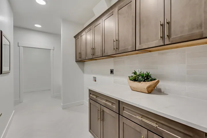 Laundry area featuring extensive upper and lower cabinetry with gold-tone hardware, a light-toned countertop, and a tiled backsplash