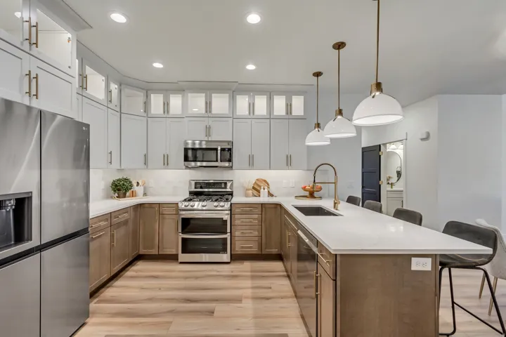 Contemporary kitchen featuring two-tone cabinetry, stainless steel appliances, a large island with sink, pendant lighting, and wood-finish flooring