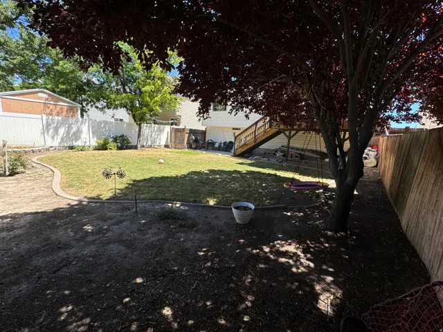 Spacious backyard featuring a manicured lawn, established shade trees, a raised wood deck, and perimeter fencing