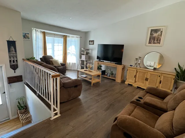 Spacious living area featuring wood-finish flooring, a large window with privacy blinds, and a white railing overlooking a lower level