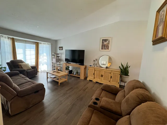 Spacious living area featuring wood-finish flooring, vaulted ceilings, and large windows with privacy blinds