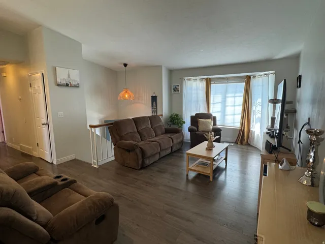 Spacious living area featuring wood-finish flooring, a bay window with blinds, and white trim throughout